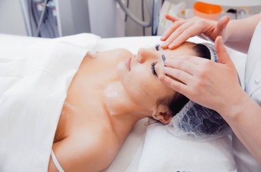 Yüz masajı. Güzellik salonunda masaj yaptıran genç bir kadının yakın çekimi. Kaplıca ve vücut bakımı. Yüz güzelliği tedavisi. Kozmetoloji.