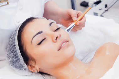 Yüz bakımı. Güzellik uzmanı güzellik salonundaki fırçayla yüzüne güzellik maskesi takıyor. Güzellik Kliniği 'nde kadın müşterinin susuzluk giderme prosedürüne yakın çekim. Kozmetoloji