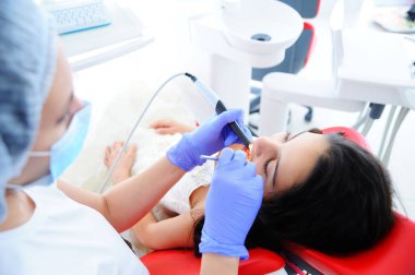 Diş muayenehanesinde genç ve güzel bir kız. Çocuk dişçisi çocuğun dişlerini muayene eder..