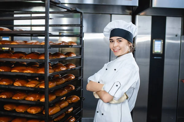 Portrait of a young baker girl on the background of an industrial oven with pastries in a bakery.