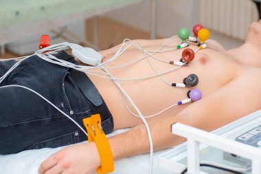 Kalbin kardiyogramı. Göğsünde elektrokardiyografın bağlı olduğu bir kanepede oturan genç bir adam. Kardiyoloji