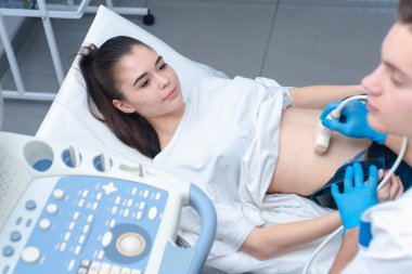 Genç doktor genç ve güzel bir kıza karın boşluğunun ultrasonunu yapar. Ultrason hamileliği