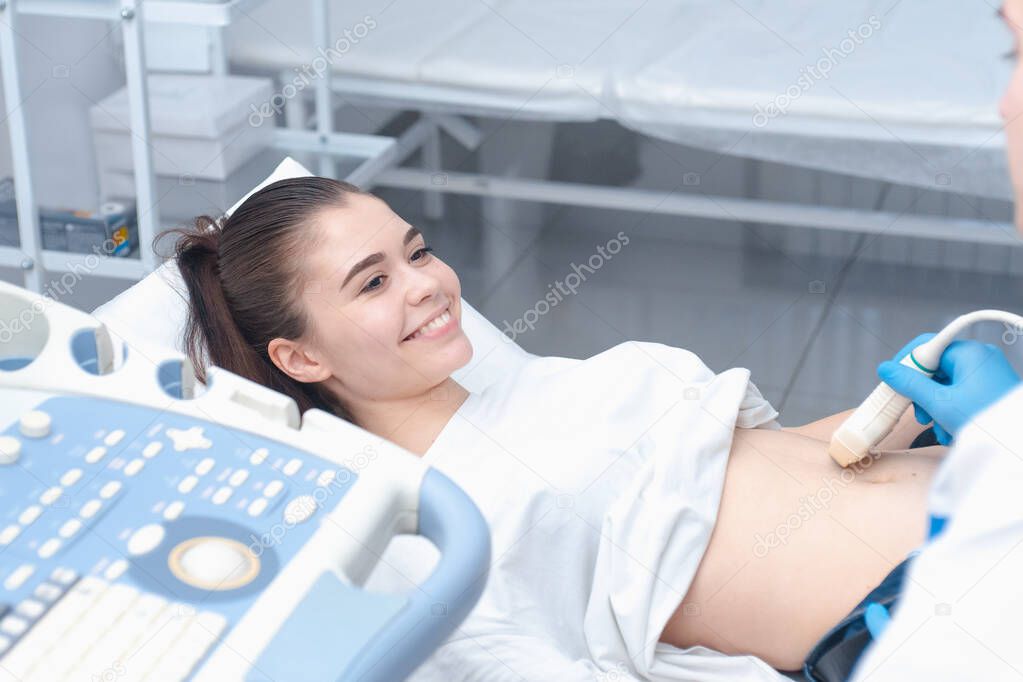 The young doctor makes an ultrasound of the abdominal cavity to a young beautiful girl. Ultrasound pregnancy