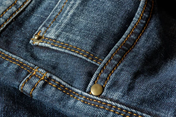 Mavi jeans turuncu dikiş ile bir parça Close-up. Perçin yakın çekim ile cep.