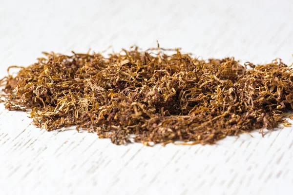 Beyaz ahşap bir masa üzerinde doğal sigara tütün yığını. Nikotin bağımlılığı. Sa˜l'k.