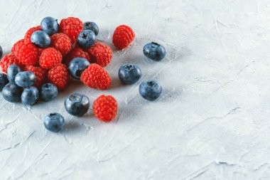 Yaban mersini ve ahududu gri çimento zemin üzerine. Olgun ve sulu taze ahududu ve yaban mersini yakın çekim. Bir sürü çilek yakın çekim.