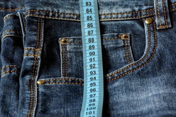 蓝色牛仔裤和一条蓝色的卷尺特写 尺寸测量 饮食和健康 — 图库照片