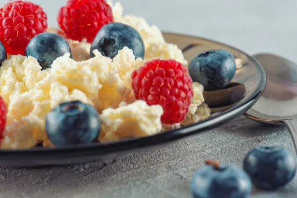 Cottage cheese with fresh raspberries and blueberries in a plate for a healthy breakfast with ripe berries. A natural healthy product.