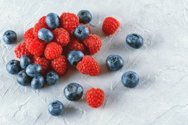 Yaban mersini ve ahududu gri çimento arka plan üzerinde karıştırın. Olgun ve sulu taze ahududu ve yaban mersini yakın çekim. Bir sürü çilek yakın çekim.