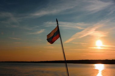 Rus bayrağı bayrak direği üzerinde zemin nehir ve gökyüzü karşı gün batımında uçar. Bağımsızlık ve vatanseverlik özgürlüktür.