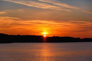 Parlak ve renkli gün batımı Nehri üzerinde. Güneş ağaçların arkasında akşam gizler. Su üzerinde batan güneşin parlamasını.