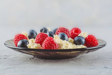 Taze ahududu ve yaban mersini olgun çilek ile sağlıklı bir kahvaltı için bir tabak içinde süzme peynir. Doğal sağlıklı bir ürün.