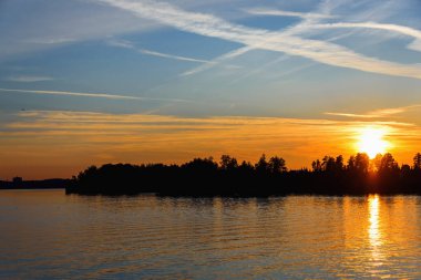 Parlak ve renkli gün batımı Nehri üzerinde. Güneş ağaçların arkasında akşam gizler. Su üzerinde batan güneşin parlamasını.