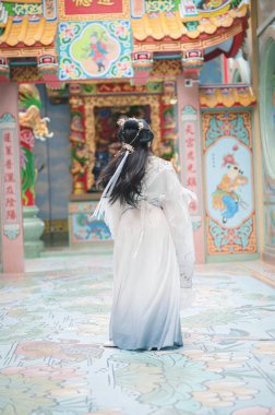A young woman dressed in elegant Hanfu attire stands gracefully in a vibrant Chinese temple, surrounded by intricate decor and colorful elements that reflect traditional culture.