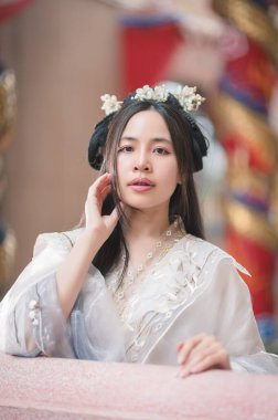 A young woman in a beautiful traditional Chinese Hanfu outfit with floral accessories poses gracefully, embodying elegance and cultural beauty in a serene setting.