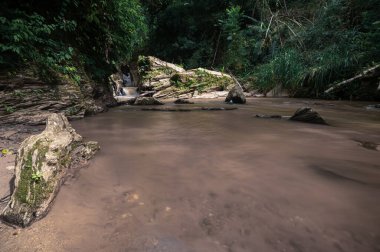 This serene image captures the flowing water of Mok Fa Waterfall in Chiang Mai, Thailand, surrounded by lush greenery and rugged rocks, perfect for nature lovers.