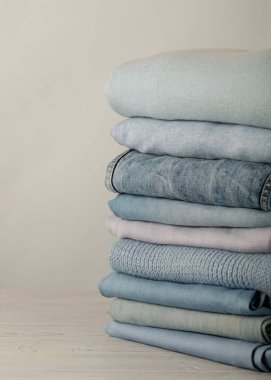 Kot pantolon ve örme giyim (kazak, eşarplar, pullovers) mavi, beyaz ve gri renkler yığını. Seçici odak.