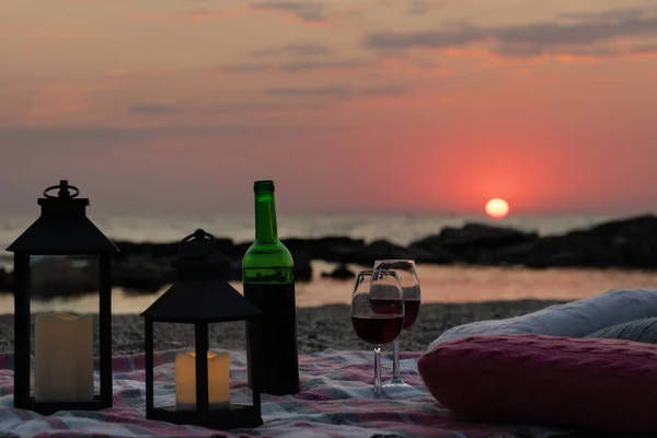 Summer sea sunset. Romantic picnic on the beach. Bottle of wine, glasses, candles, plaid and pillows. Selective focus.