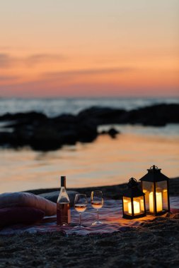 Yaz deniz günbatımı. Sahilde romantik piknik. Bir şişe şarap, Gözlük, mumlar, ekose ve yastıklar. Seçici odak.