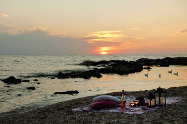 Yaz deniz günbatımı. Sahilde romantik piknik. Bir şişe şarap, Gözlük, mumlar, ekose ve yastıklar. Seçici odak.
