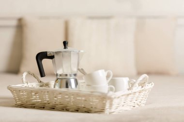 Yatakta kahvaltı. Bir beyaz hasır tepsi üzerinde bir kahve makinesi, kahve beyaz fincan vardır. Seçici odak.