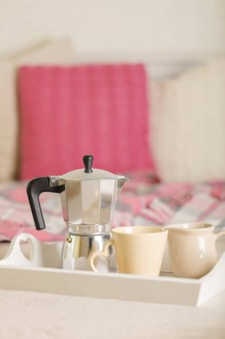 Yatakta kahvaltı. Bir beyaz hasır tepsi üzerinde bir kahve makinesi, kahve kupa ve kruvasan işte. Seçici odak.