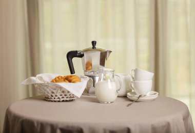 Kahve makinesi, bardak ve kruvasan sepet bir yuvarlak masa pencerenin önünde bulunmaktadır. Seçici odak.