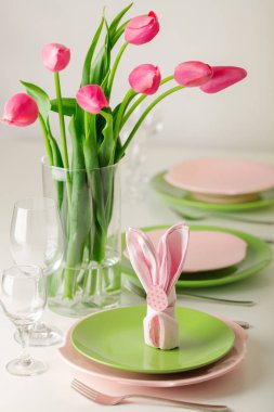 Mutlu Paskalyalar. Dekor ve Paskalya tablonun tablo ayarını pembe laleler ve yemekleri pembe ve yeşil renk ile bir vazo var. Seçici odak.