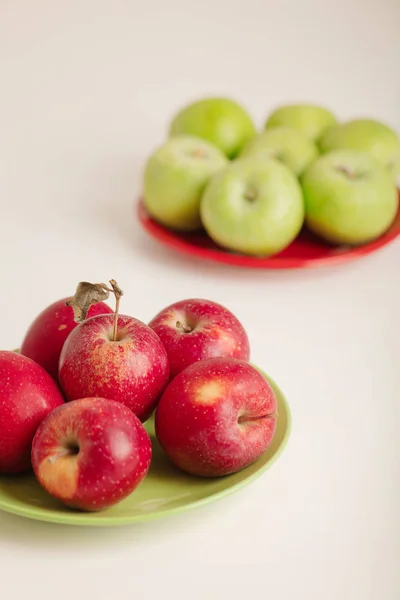 Red and green apples on a plate on a white background. Selective focus.