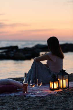 Yaz deniz günbatımı. Sahilde romantik piknik. Bir şişe şarap, Gözlük, mumlar, ekose ve yastıklar. Seçici odak.