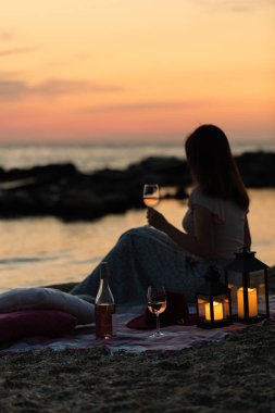 Yaz deniz günbatımı. Sahilde romantik piknik. Bir şişe şarap, Gözlük, mumlar, ekose ve yastıklar. Seçici odak.