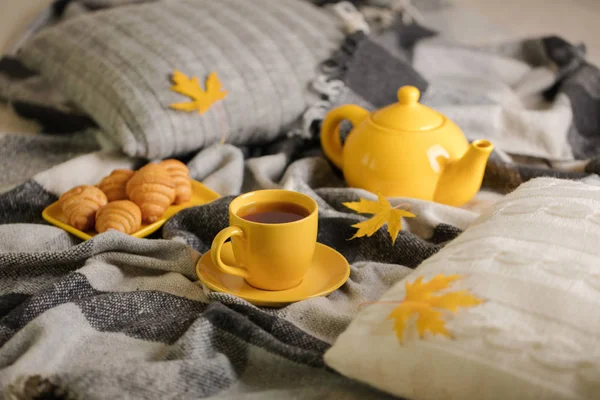 Home comfort and warmth in the autumn time. Gray plaid, knitted pillows, tea and autumn maple leaves. Selective focus.