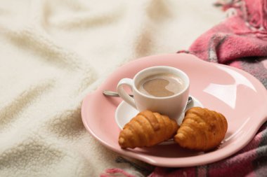 Kış zamanı. Rahat, sıcak ve pembe bir battaniye ve bir fincan kahve ve kruvasan yatakta. Seçici odak.