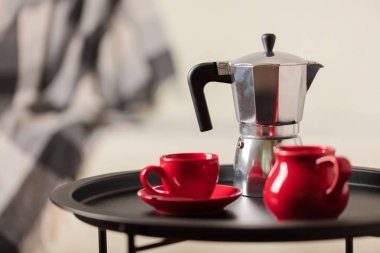 Yuvarlak siyah metal sehpa ile kahve makinesi ve beyaz kanepe gri bir battaniye ile arka planda bir fincan. Seçici odak.