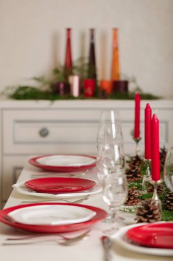 Mutlu Noeller ve mutlu yeni yıl! Masa şenlikli dekorasyonu - beyaz ve kırmızı ayarlama yemekleri, şamdanlar, ardıç dalları ve çam kozalakları kırmızı mumlar. Seçici odak.