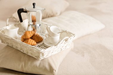 Yatakta kahvaltı. Bir beyaz hasır tepsi üzerinde bir kahve makinesi, kahve beyaz bardak ve kruvasan işte. Seçici odak.