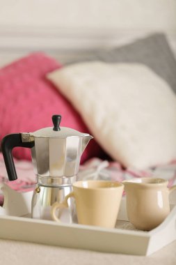 Yatakta kahvaltı. Bir beyaz hasır tepsi üzerinde bir kahve makinesi, kahve kupa ve kruvasan işte. Seçici odak.