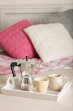 Yatakta kahvaltı. Bir beyaz hasır tepsi üzerinde bir kahve makinesi, kahve kupa ve kruvasan işte. Seçici odak.