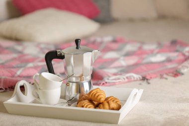 Yatakta kahvaltı. Bir beyaz hasır tepsi üzerinde bir kahve makinesi, kahve kupa ve kruvasan işte. Seçici odak.