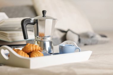 Yatakta kahvaltı. Beyaz bir tepsi üzerinde bir kahve makinesi, mavi kahve ve kruvasan işte. Seçici odak.