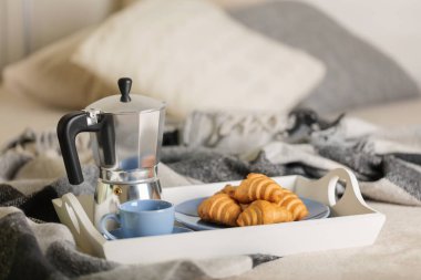 Yatakta kahvaltı. Beyaz bir tepsi üzerinde bir kahve makinesi, mavi kahve ve kruvasan işte. Seçici odak.