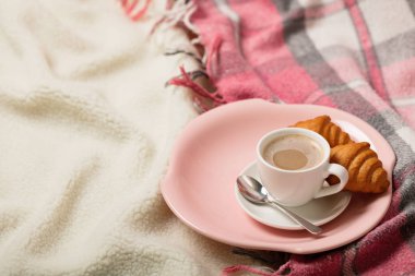 Kış zamanı. Rahat, sıcak ve pembe bir battaniye ve bir fincan kahve ve kruvasan yatakta. Seçici odak.