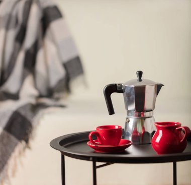 Yuvarlak siyah metal sehpa ile kahve makinesi ve beyaz kanepe gri bir battaniye ile arka planda bir fincan. Seçici odak.