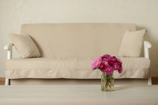 Beige sofa with pillows in the living room and vase with Flowers (Michaelmas daisy, asters). Selective focus.