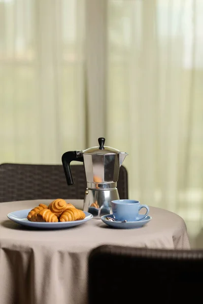 Coffee maker, cups and croissants in the basket are on a round t