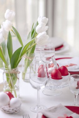 Mutlu paskalyalar. Paskalya tablonun Tablo ayarı ve dekor Beyaz Lale ve kırmızı ve beyaz renkteki yemekleri ile bir vazo var. Paskalya yumurta ile beyaz lekeli renkli. Seçici odak.