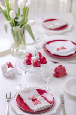 Mutlu paskalyalar. Paskalya tablonun Tablo ayarı ve dekor Beyaz Lale ve kırmızı ve beyaz renkteki yemekleri ile bir vazo var. Paskalya yumurta ile beyaz lekeli renkli. Seçici odak.