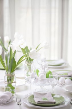 Paskalya tablonun Tablo ayarı ve dekor beyaz laleler ve yemekleri yeşil ve beyaz renk ile bir vazo var. Paskalya dekor ile beyaz lekeli. Seçici odak.