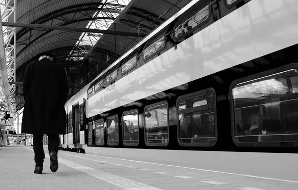 老人低着头走在黑白相间的空荡荡的站台上, 沿着火车走着 — 图库照片