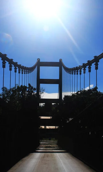 Imagem de uma ponte metálica mostrando uma linha de cabos e um céu azul brilhante com o sol no céu — Fotografia de Stock